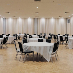 Empty banquet hall with round tables draped in white cloths and black chairs arranged for an event.