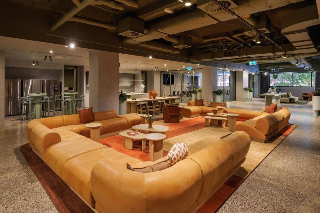 Open-concept office lounge with large orange sectional sofas around circular coffee tables on a patterned rug, spacious and bright.