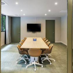 Conference room with a long wooden table and tan swivel chairs, and a wall-mounted TV on the far wall.