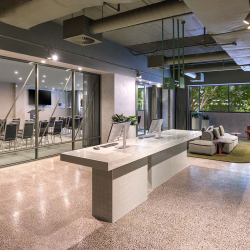 Modern office lobby with a marble reception desk, glass-walled conference rooms on the left, and a seating area with sofas on the right.