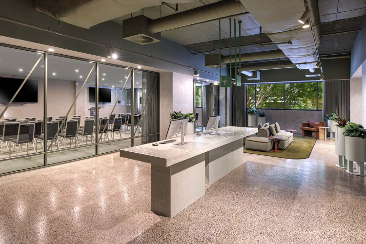 Modern office lobby with a marble reception desk, glass-walled conference rooms on the left, and a seating area with sofas on the right.