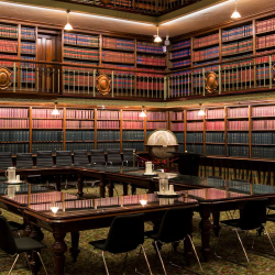 Elegant library conference room with a large wooden table, black chairs, and floor-to-ceiling leather-bound books.