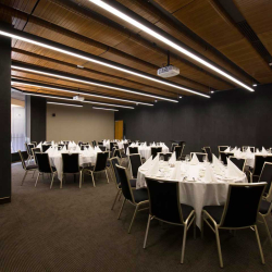 Banquet hall set for a formal dinner with round tables, white tablecloths, folded napkins, and black chairs.