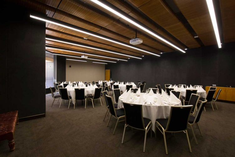 Banquet hall set for a formal dinner with round tables, white tablecloths, folded napkins, and black chairs.