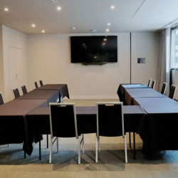 Conference room with black-clothed tables arranged in a U-shape and seating for about a dozen, a wall-mounted flat-screen TV, and large windows on the right.