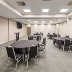 Empty conference room with round tables covered in black cloth and gray chairs, a podium, and wall-mounted TVs in the background.