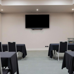 Conference room with black-tablecloth tables arranged for a presentation and a wall-mounted TV at the front.