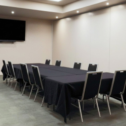 Conference room with a long U-shaped table covered in black cloth, surrounded by chairs, and a large wall-mounted TV at the front.