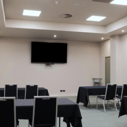 Empty conference room with tables covered in black cloths and a wall-mounted TV screen above.