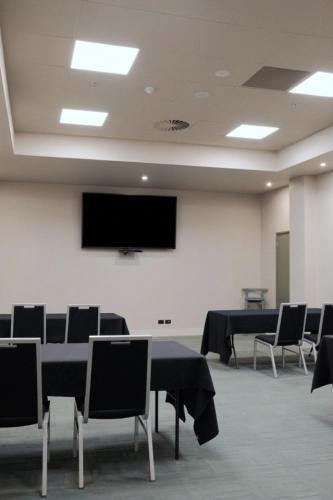 Empty conference room with tables covered in black cloths and a wall-mounted TV screen above.
