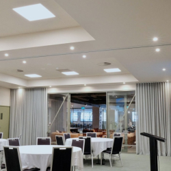 Event space set for a gathering with round tables in white cloths, black chairs, and a black podium on the right.