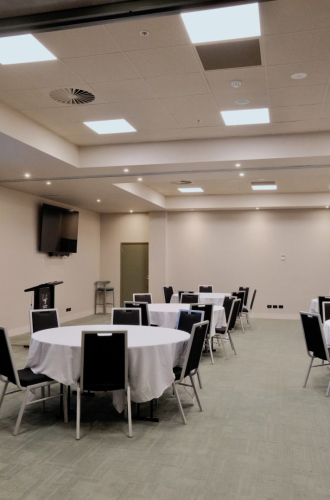 Banquet-style conference room with round tables covered in white cloths and black chairs around them.